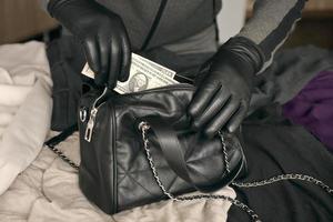 rånare i svart utrusta och handskar ser i öppnad stulen kvinnor väska. de tjuv tar ut oss dollar räkningar från en kvinnors handväska i kök foto