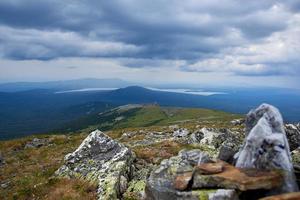 grön bergen täckt med skog, storm moln, se från de topp med stenar foto