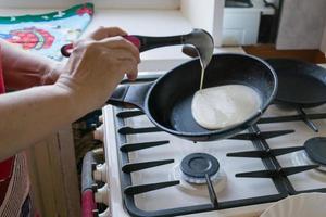 de deg sprider sig i en panorera för bakning pannkakor i de händer av ett äldre kvinna foto