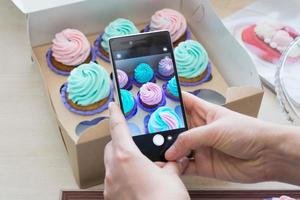 fotografering en låda med muffins med en telefon förbi kvinnors händer foto