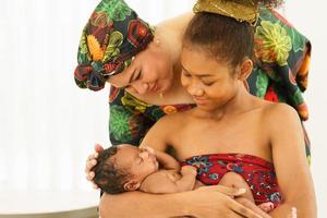 mor och äldst dotter i traditionell klänning inhemsk stil afrikansk bära nyfödd bebis en månad gammal amning. Lycklig spädbarn blandad lopp afro-asien sömn väl i värma omfamning av moderskap. foto