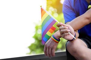 regnbåge flagga hålning i hand av asiatisk Gay som bär regnbåge handledsband till ring upp ut och visar HBTQ kön mångfald och respekterar kön alternativ runt om de värld. foto