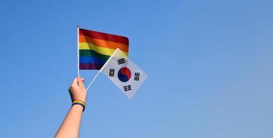 söder korea flagga och regnbåge flagga höjning i händer och mot blå himmel, mjuk och selektiv fokus, begrepp för HBTQ fester och HBTQ evenemang i stolthet månad i söder korea. foto