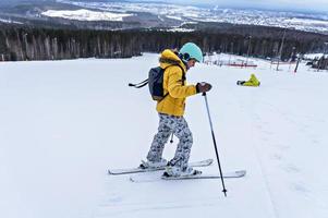 ung kvinna i gul jacka och åka skidor hjälm skidåkning ner på berg backe, vinter- sporter, alpina skidåkning utomhus aktivitet, friska livsstil foto