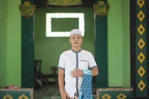 ung asiatisk muslim bön- i de moské bärande en bön matta foto