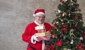 senior caucasian man fira jul i lycka och spänning medan innehav de närvarande bredvid fullt dekorerad jul träd foto