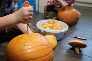 halloween förberedelse. familj träsnideri pumpa in i Pumpalykta medan Sammanträde på de golv, i de hus. foto