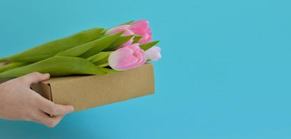 vår blommor. händer innehav rosa tulpaner på en låda. grattis. de begrepp av vår gåvor och högtider foto