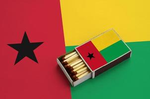 guinea bissau flagga är visad i ett öppen tändsticksask, som är fylld med tändstickor och lögner på en stor flagga foto