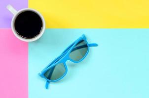 små vit kaffe kopp och blå solglasögon på textur bakgrund av mode pastell blå, gul, violett och rosa färger papper i minimal begrepp foto