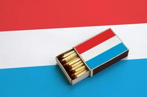 luxemburg flagga är visad i ett öppen tändsticksask, som är fylld med tändstickor och lögner på en stor flagga foto