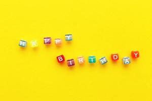 Lycklig födelsedag inskrift tillverkad av färgrik kuber pärlor på gul bakgrund foto