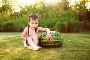 porträtt av Lycklig barn pojke med en stor hela vattenmelon i de tillbaka gård foto