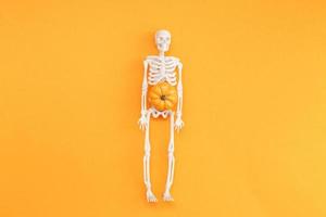 skelett med pumpa på orange bakgrund. halloween begrepp foto
