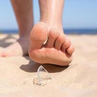 ben promenader på de strand och kör de risk av skada, stepping på en skärva av bruten glas, som är liggande på de sandig stranden. foto