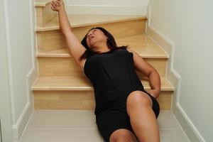 asiatisk lady kvinna skada från faller ner på hal ytor trappa på Hem. foto