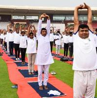 ny delhi, Indien, juni 21 2022 - grupp yoga övning session för människor på yamuna sporter komplex i delhi på internationell yoga dag, stor grupp av vuxna delta yoga klass i cricket stadion foto