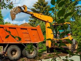 orange grävmaskin lossar sand från en dumpa lastbil. gräv i de jordbruks område. foto