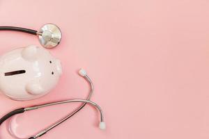 medicin läkare utrustning stetoskop och spargris isolerad på rosa pastell bakgrund. hälsovård finansiell kontroll eller spara för sjukförsäkring kostnader koncept. platt låg ovanifrån kopia utrymme. foto
