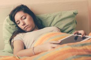 ung kvinna somnar medan du använder den digitala minnestavlan på sängen