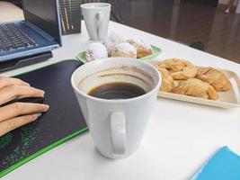 en ung kvinna drack en glas av kaffe åtföljs förbi snacks under bryter under arbete tid. foto