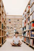 barn i skola bibliotek. barn läsa böcker. liten pojke läsning och studerar. barn på bok Lagra. smart intelligent förskola unge välja böcker till låna. foto