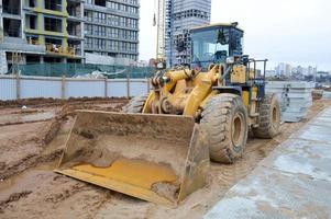 stor ljus gul kraftfull industriell tung grävmaskin traktor, bulldozer, specialiserade konstruktion Utrustning för väg reparera under de konstruktion av en ny mikrodistrikt i en stor stad foto