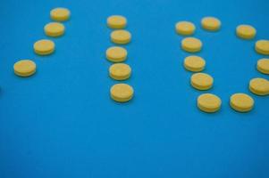 volumetriska gul piller skott på en blå bakgrund i de form av brev. mediciner hällde från en kan är skott från ovan på färgad bakgrunder. engelsk alfabet i de form av tabletter foto
