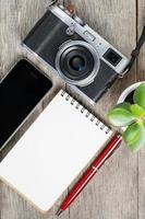 klassisk kamera med tom anteckningsblock sida och röd penna på grå trä, årgång skrivbord med telefon. foto