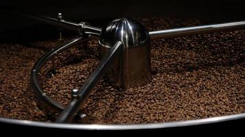 kaffe rosten maskin på kaffe rostning bearbeta. blandning kaffe bönor. rostad spinning kylare professionell maskiner och färsk brun kaffe bönor rörelse närbild mörk Foto på fabrik.
