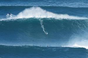 surfare är ridning en jätte stor Vinka nära de fort av sao miguel arcanjo fyr i nazare, portugal. största vågor i de värld. turistiska destination för surfing och älskande av radikal sporter. foto