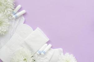 menstruations- dynor och tamponger med anbud vit blommor på pastell lila bakgrund foto