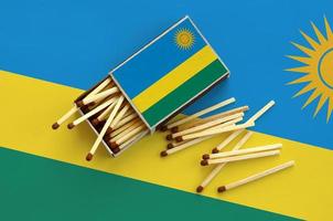 rwanda flagga är visad på ett öppen tändsticksask, från som flera tändstickor falla och lögner på en stor flagga foto