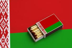 Vitryssland flagga är visad i ett öppen tändsticksask, som är fylld med tändstickor och lögner på en stor flagga foto