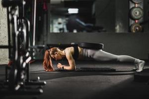 muskulös kvinna håller på med planka övningar under arbetssätt ut på de Gym foto