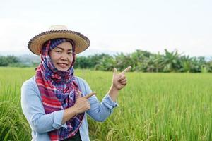 asiatisk kvinna man jordbrukare är på lantbruk landa, bär hatt, thai loincloth täckt huvud, blå skjorta och göra hand gest till närvarande något.koncept , lantbruk ockupation. jordbrukare med organisk ris. foto