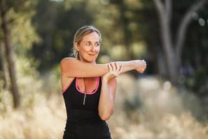 kvinna håller på med stretching övningar under Träning i parkera på sommar dag foto