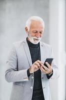 en senior företag man använder sig av smartphone medan stående i de kontor hall foto