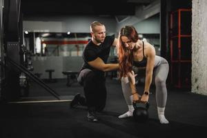 muskulös kvinna håller på med kettle Träning med personlig tränare på de Gym foto