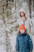 mamma och son spela snöbollar i de vinter- skog. mamma promenader med henne son i en snöfall i de skog. Lycklig vinter- högtider med snö. vinter- promenader i de skog. foto