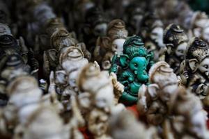 de sten statyett av ganesh är grön, kontrasterande med de grupp av ljus ganesh på de disken av de indisk marknadsföra foto