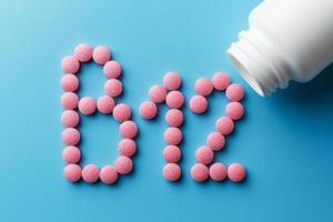 rosa piller i de form av de brev b12 på en blå bakgrund, spillts ut av en vit burk. foto