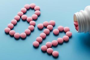 rosa piller i de form av de brev b12 på en blå bakgrund, spillts ut av en vit burk. foto