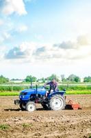 de jordbrukare enheter en traktor med en fräsning enhet Utrustning. lossna landa odling använda sig av av jordbruks maskineri till hastighet upp arbete. jordbruk. plöjning fält. de skede av framställning jord för plantering. foto