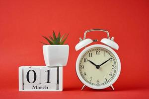 larm klocka på röd bakgrund och trä- kalender block med datum 1 Mars foto