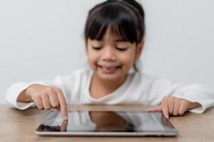 asiatisk liten söt flicka rörande de digital läsplatta skärm på de tabell foto