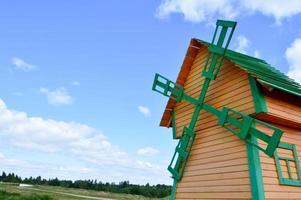 en skön trä- kvarn är en rustik naturlig väderkvarn tillverkad av styrelser av gul och grön loggar mot en blå himmel med moln foto