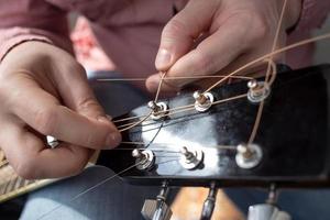 händer manlig skär ny strängar i ett akustisk gitarr. reparera av musikalisk instrument. foto