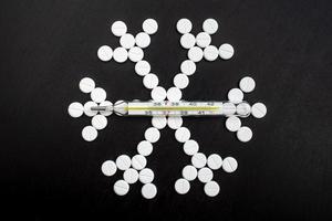snöflinga tillverkad från medicinsk piller och en termometer på en svart tabell. hälsa begrepp. topp se. foto