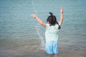 asiatisk söt flicka gående eller löpning eller spelar på de strand på sommar högtider. barn med skön hav, sand och blå himmel. Lycklig barn på semester på havet löpning på de strand. foto